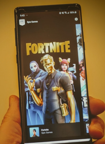 Person holding smartphone displaying Fortnite game on the Epic Store.
